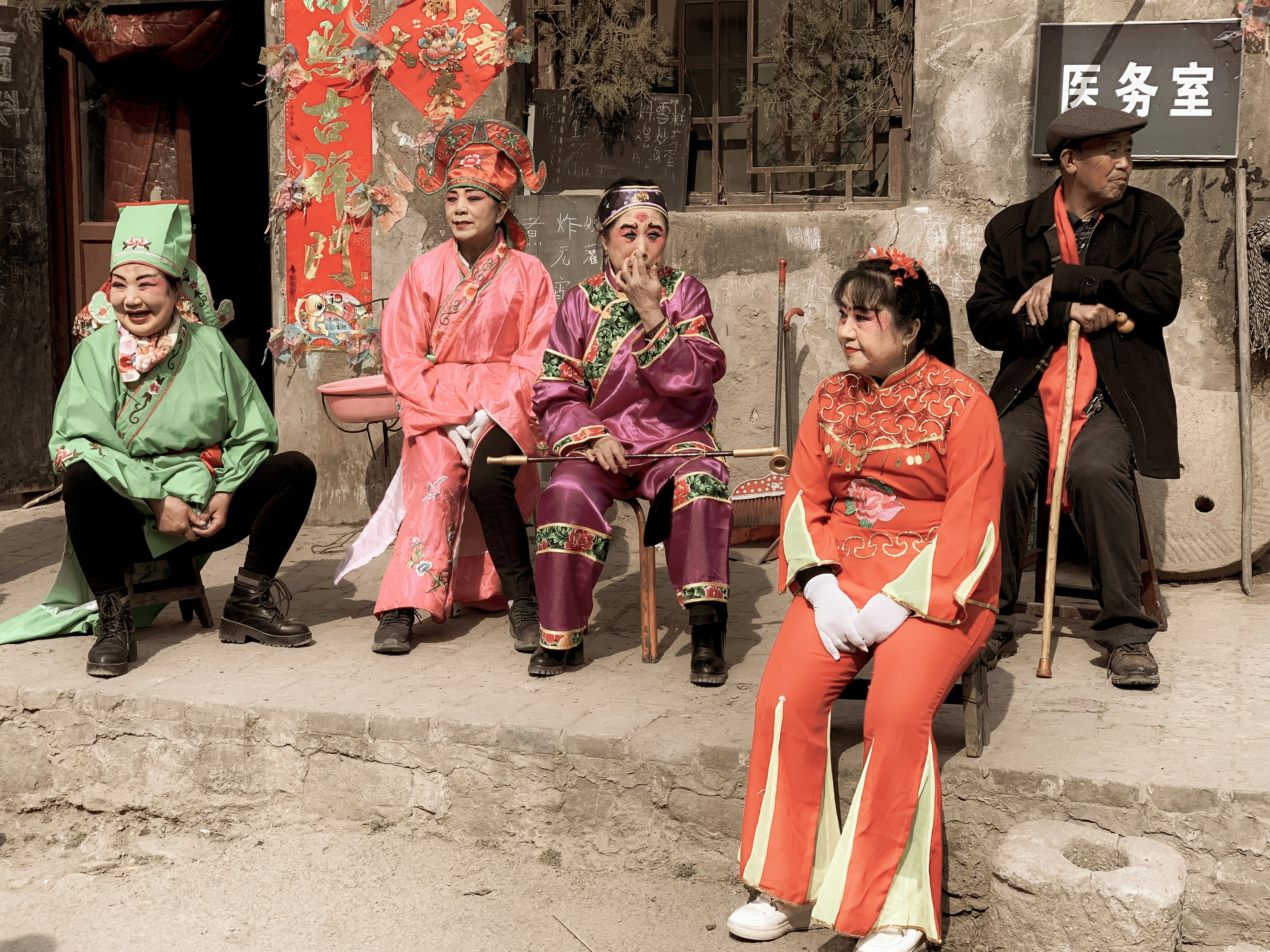 3 women in red traditional dress sitting on concrete bench